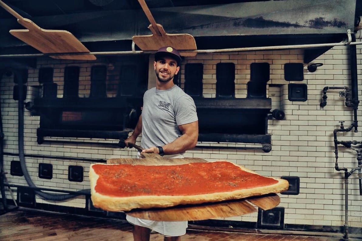 A man holding a big tomato pie at Sarcone's Bakery in Philadelphia.